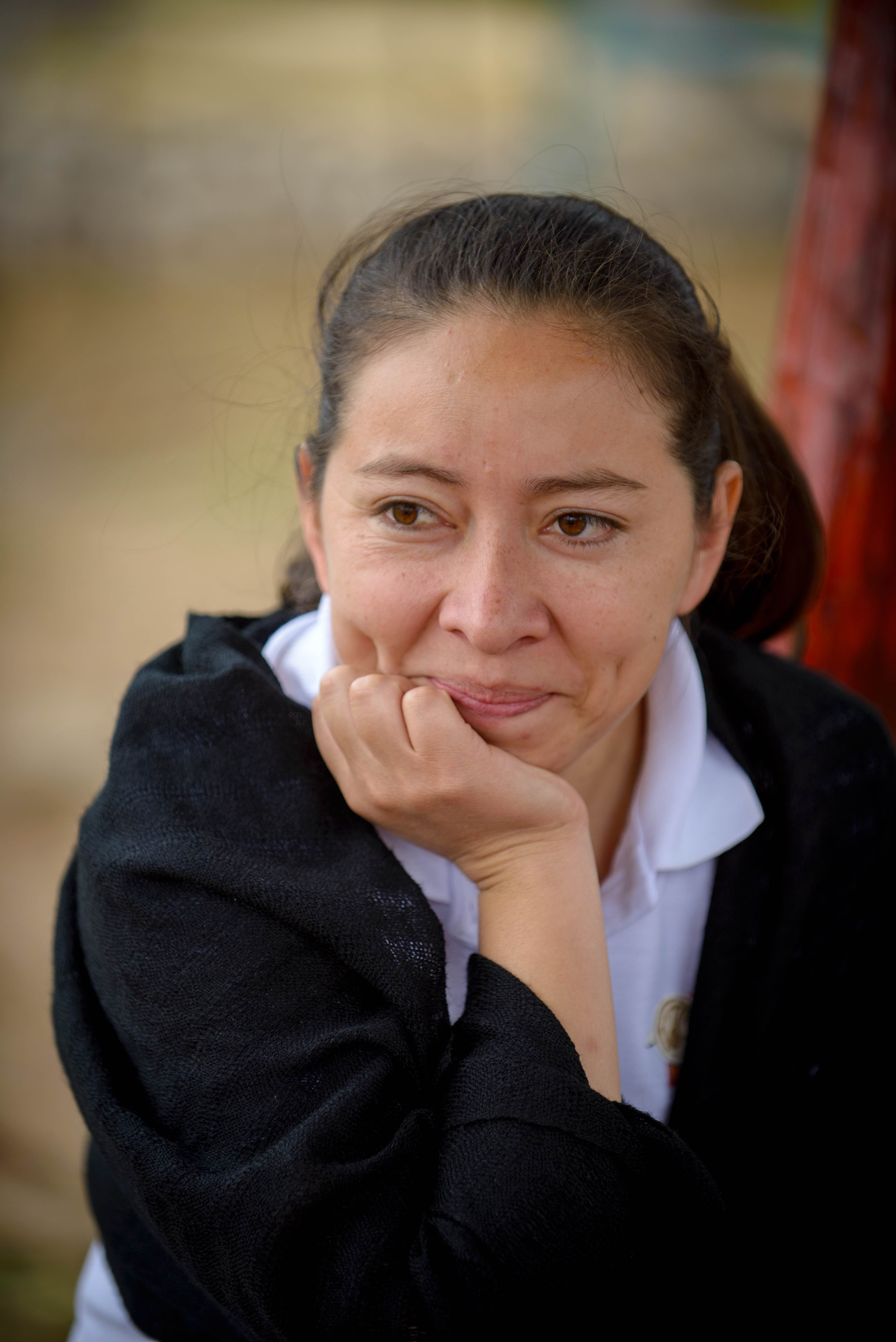 Woman from Honduras wearing a black hoodie, propping her head up with one hand while looking into the distance.