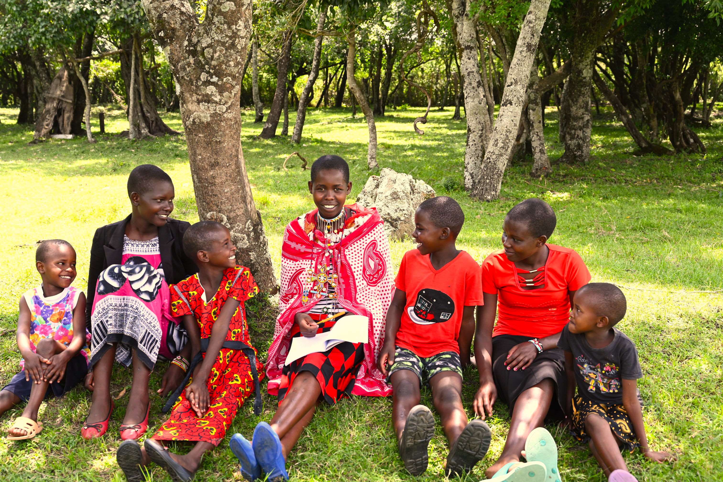 Un grupo de chicas activistas contra la MGF de Kenia se sentaron juntas en un campo verde, sonriendo.