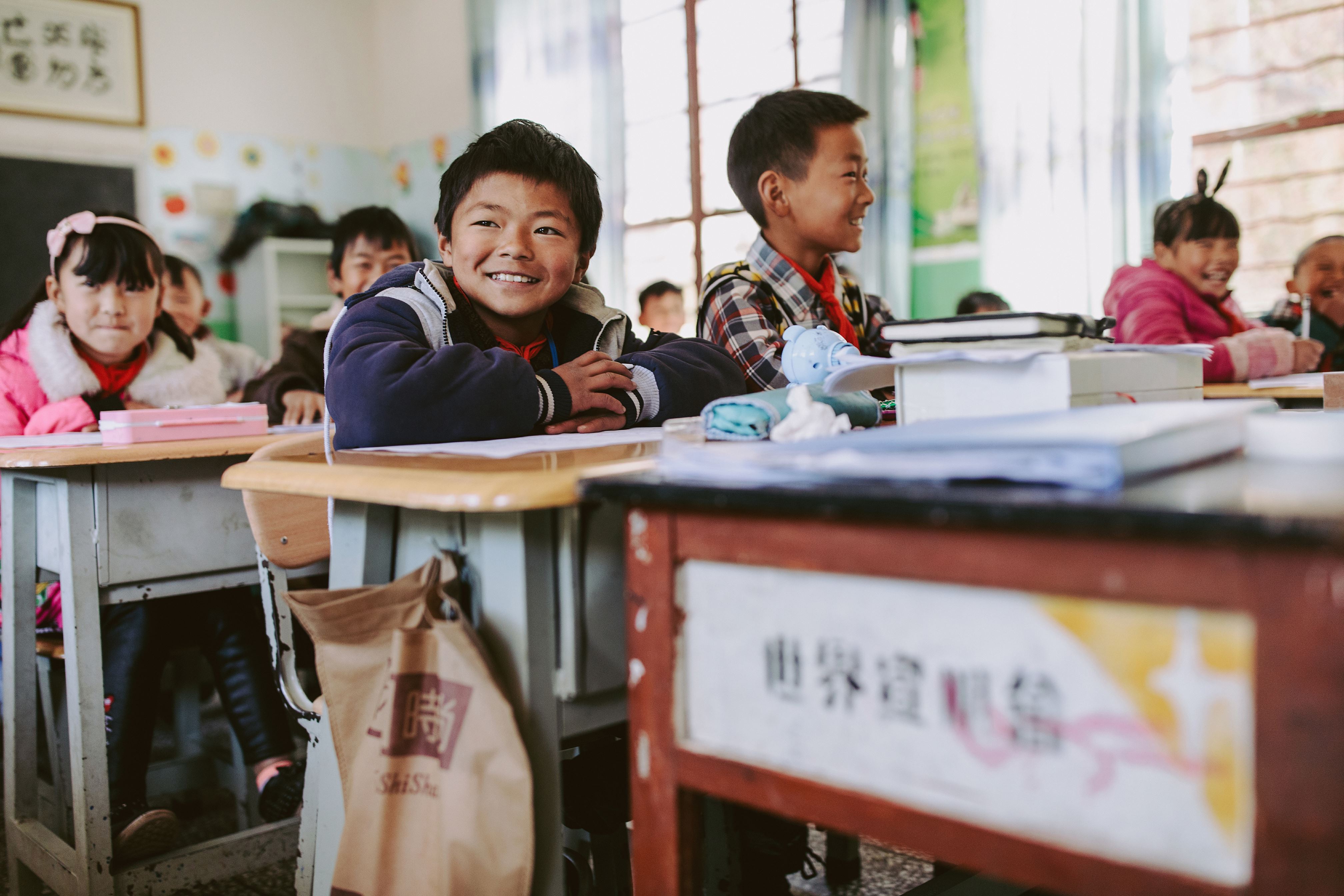 Escolar en China sentado en su pupitre y sonriendo en clase