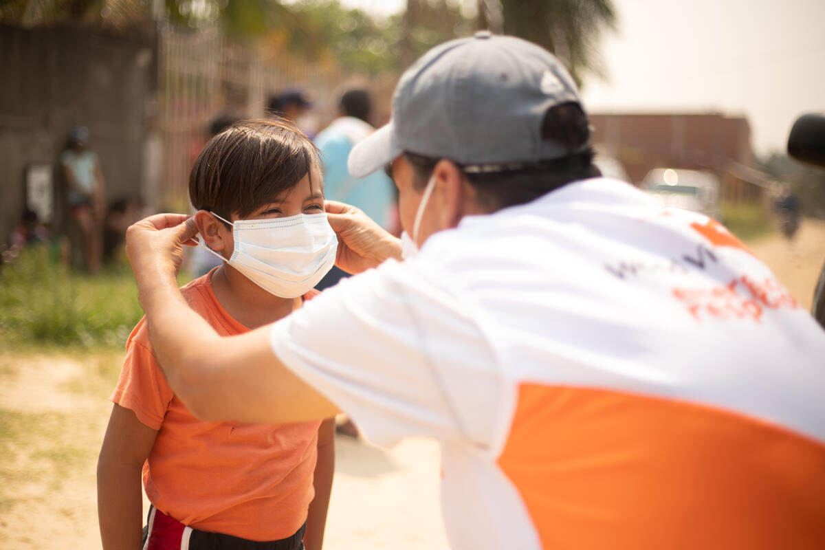 Un miembro del personal de World Vision yuda a un niño en Bolivia a ponerse una mascarilla