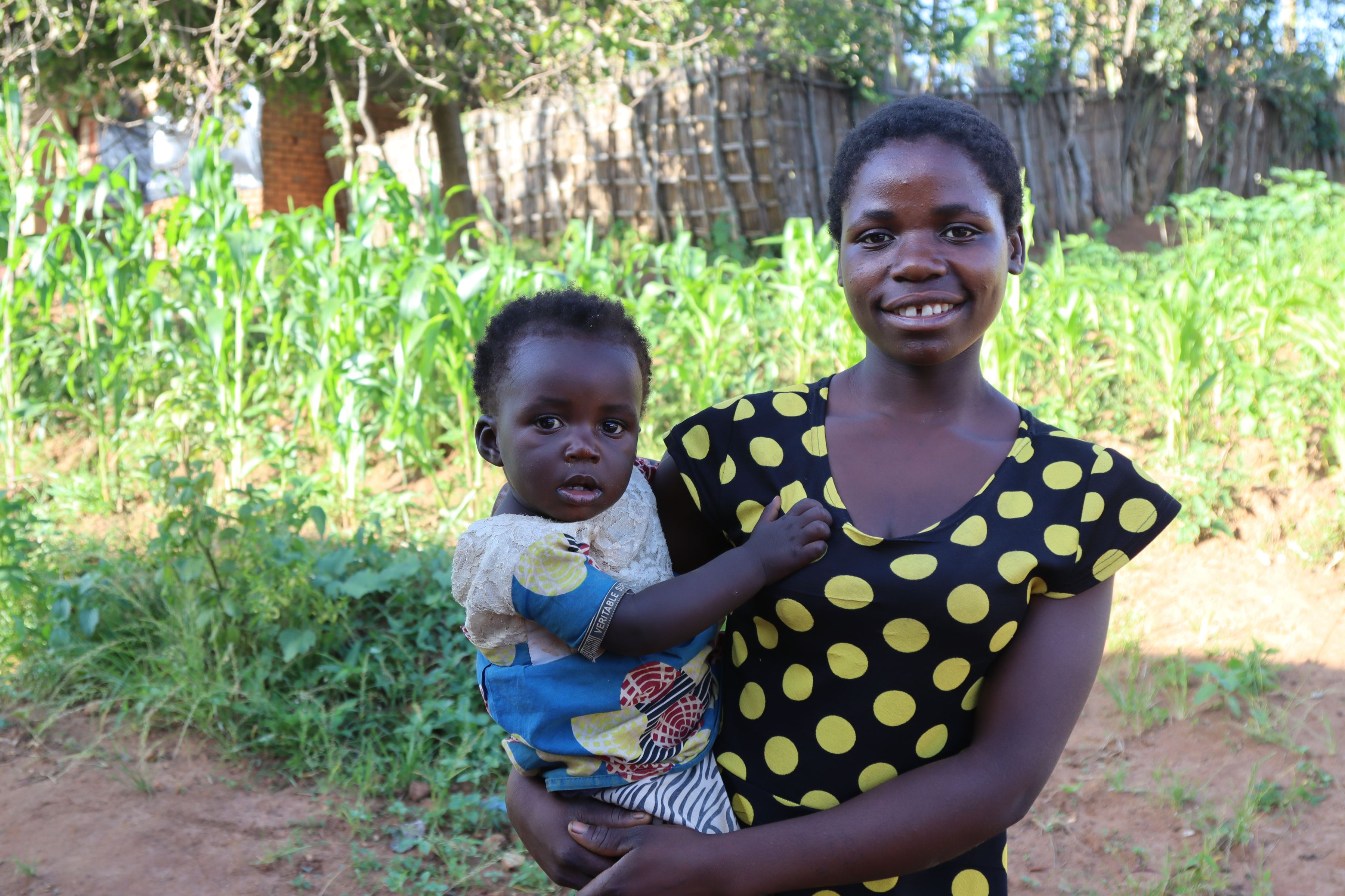 Una madre adolescente de Malawi sonríe a la cámara con su hija pequeña en brazos