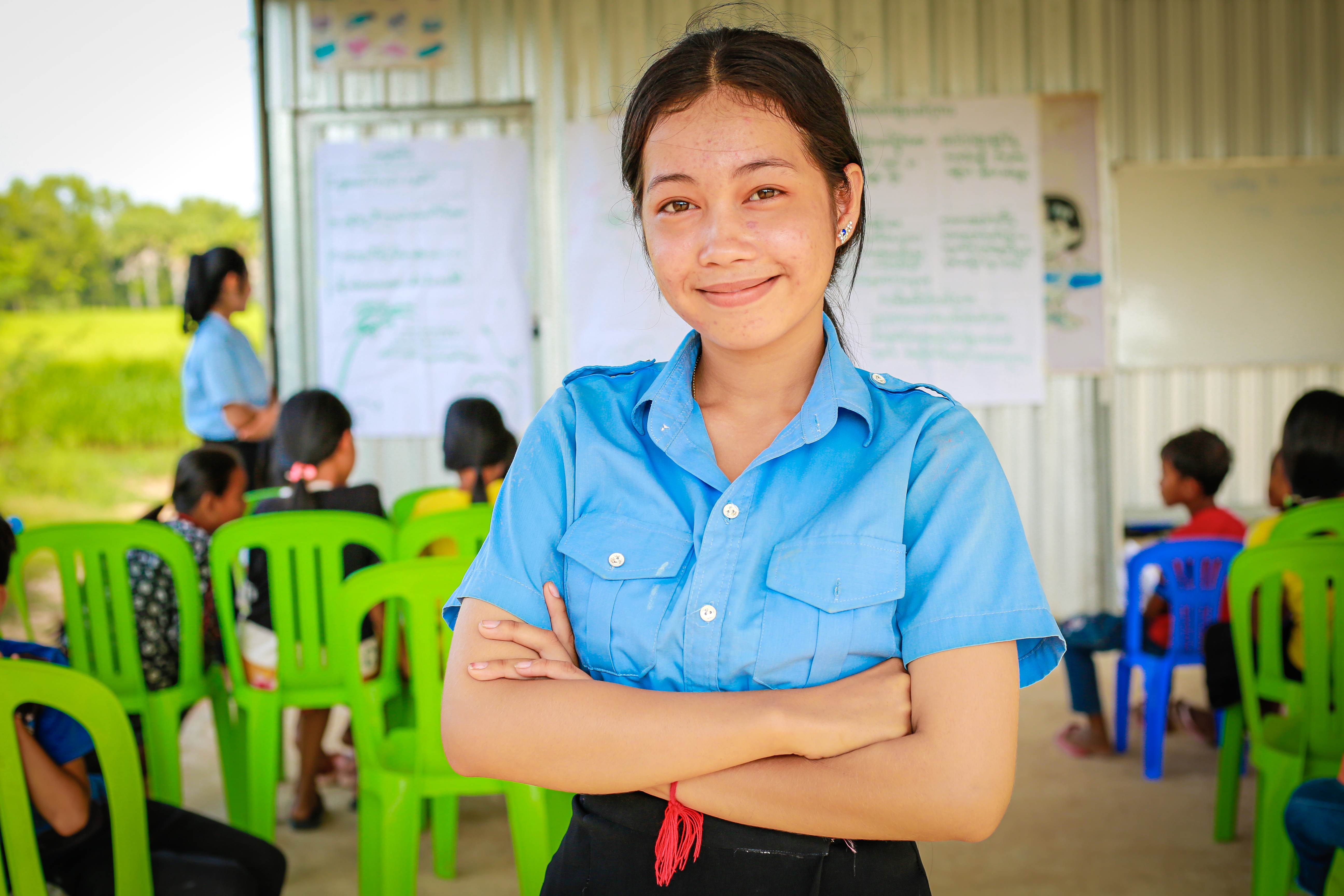 Joven defensora de Camboya sonriendo con los brazos cruzados, de espaldas a un aula