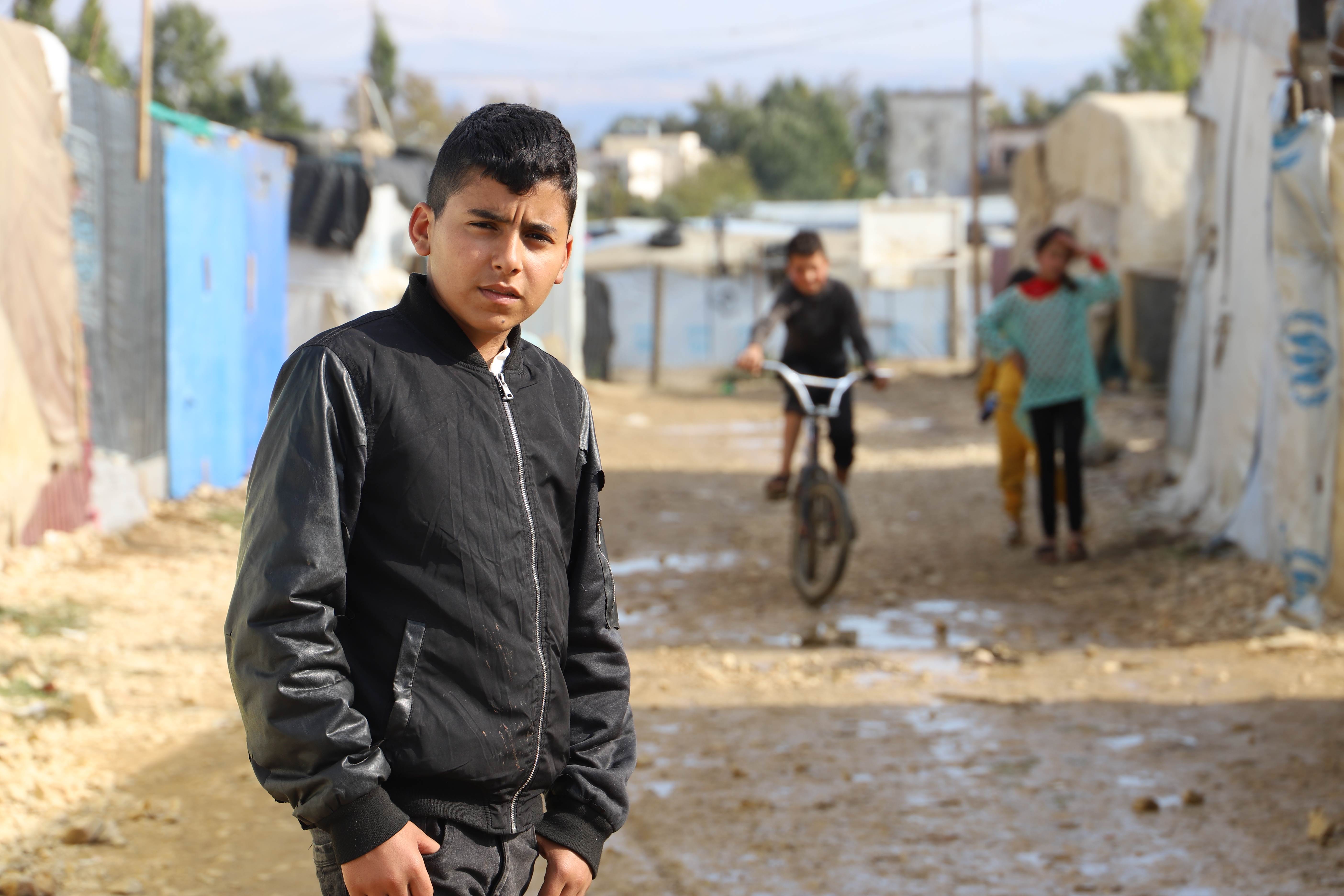 Un niño sirio frente a unas tiendas de campaña en un campo de refugiados en Siria