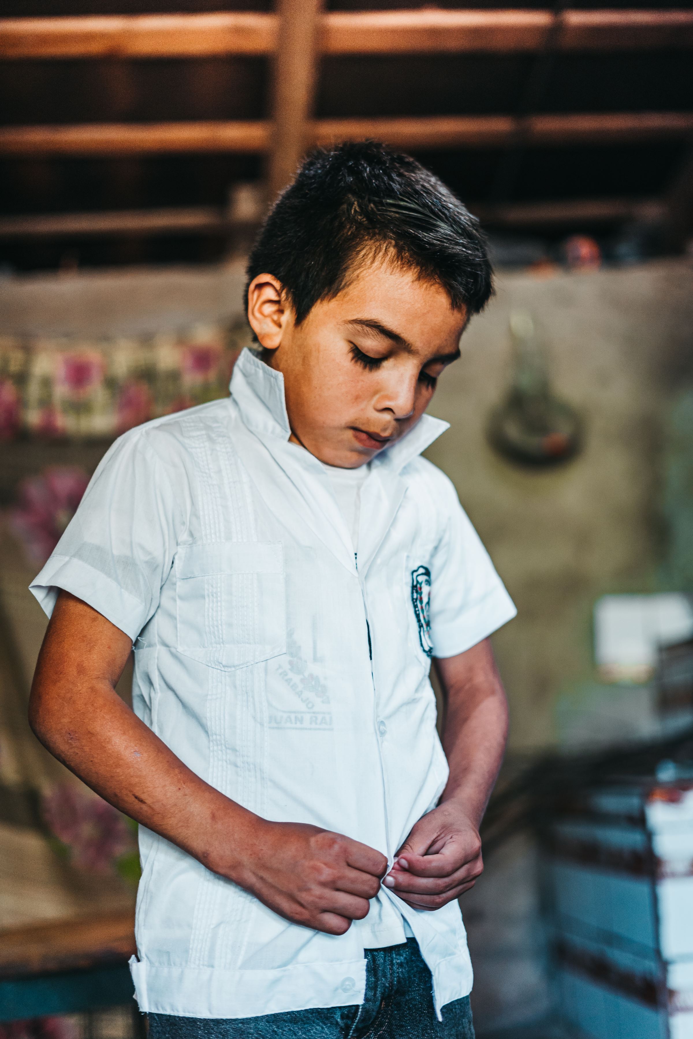 Niño hondureño con camisa de cuello blanco, mirándose las manos.