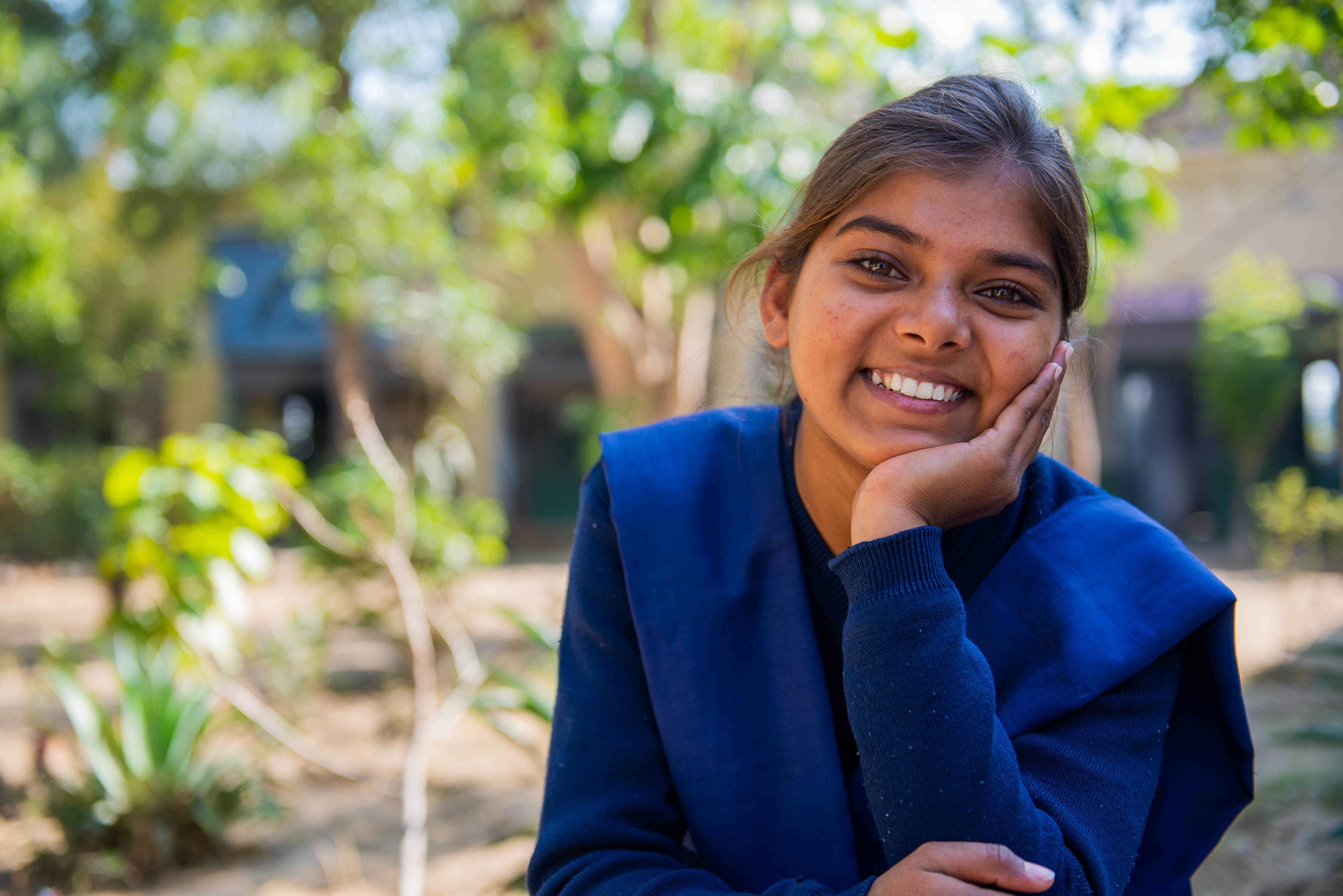 Una niña apadrinada en India sonríe a la cámara con la cabeza apoyada en la mano