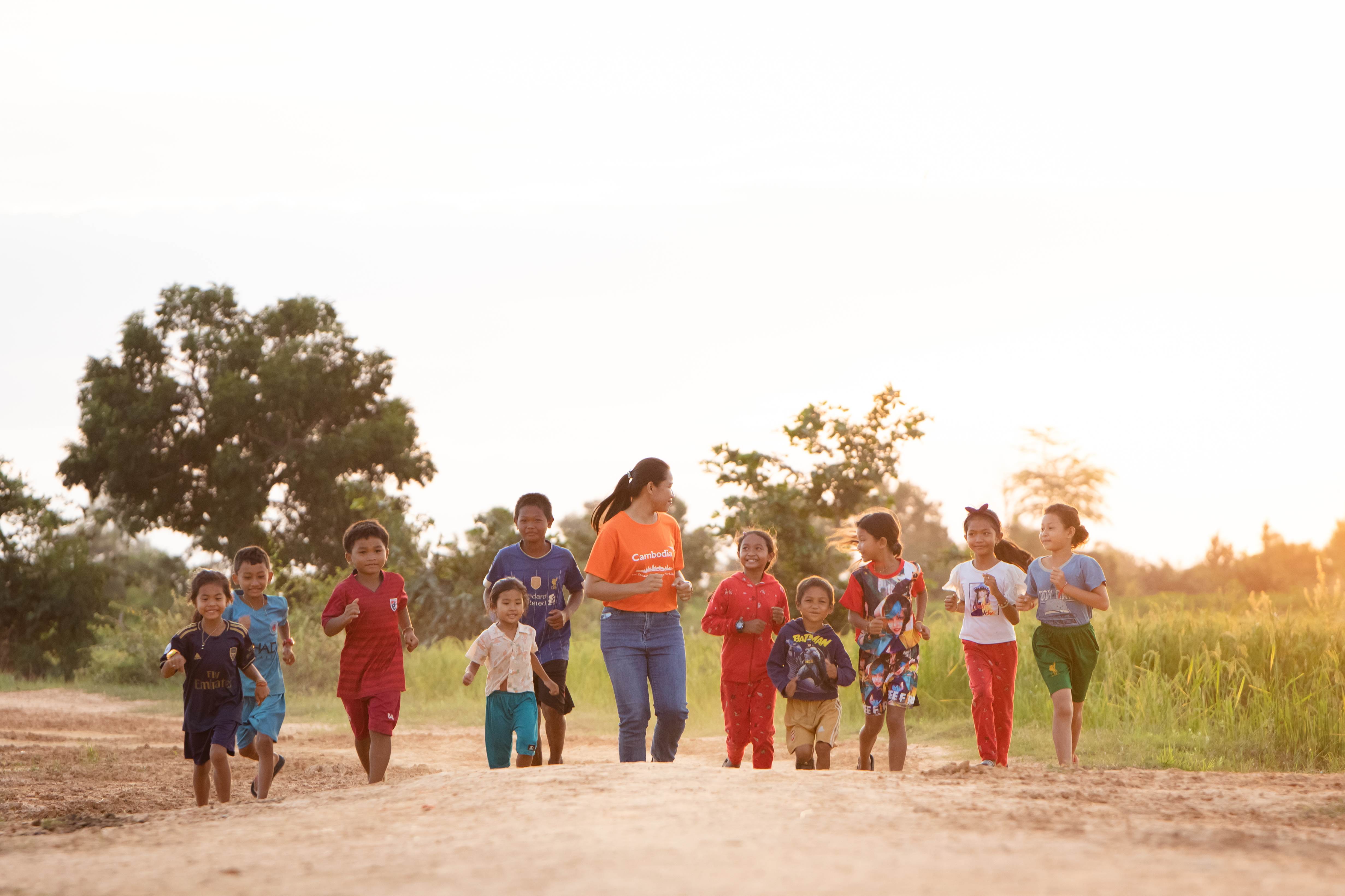 Voluntario de World Vision con un grupo de niños en Camboya, cargando tinas llenas de agua