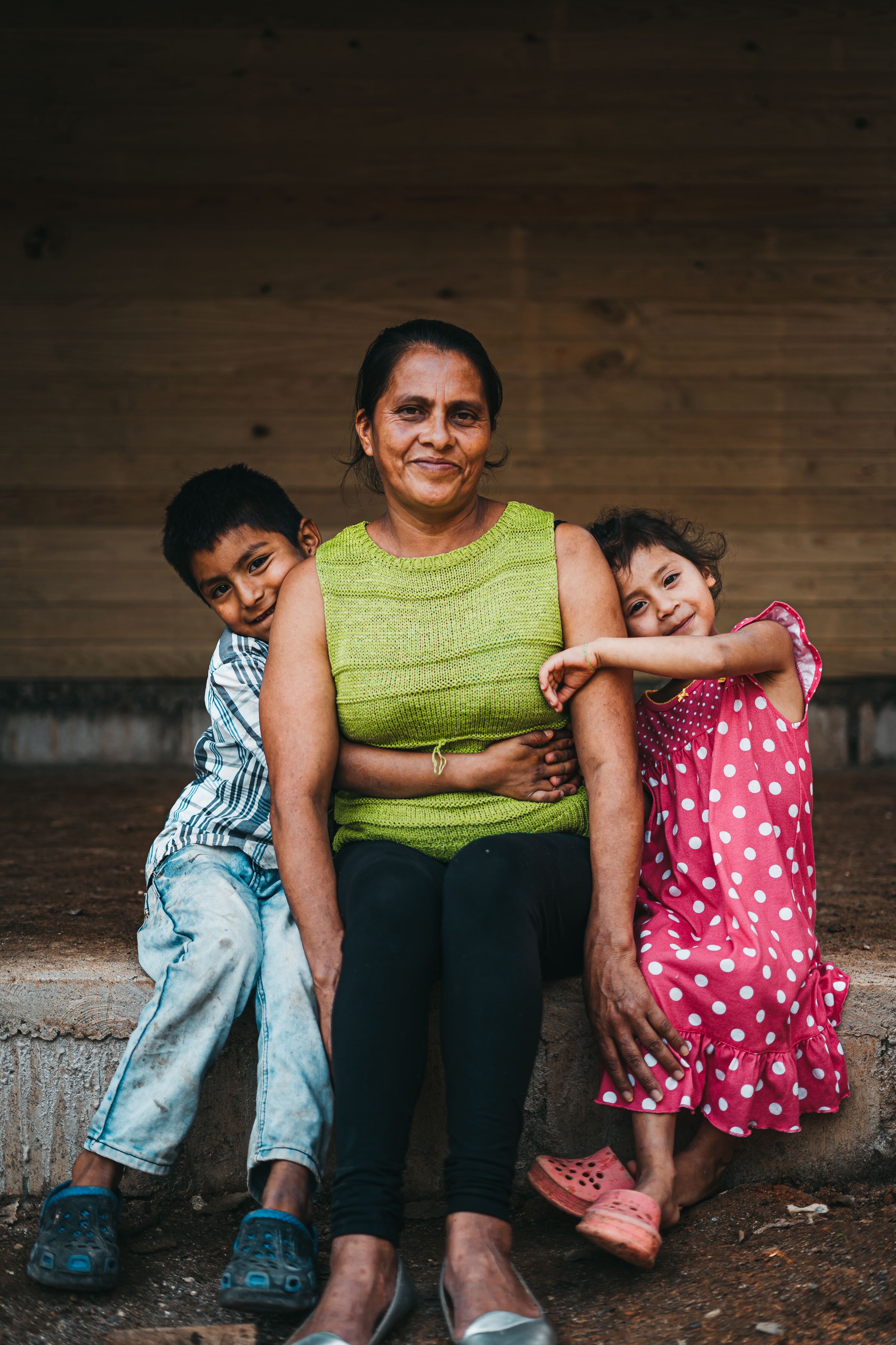 Una mujer hondureña sonríe y mira a la cámara mientras sus dos hijos, niño y niña, la abrazan por cada lado.