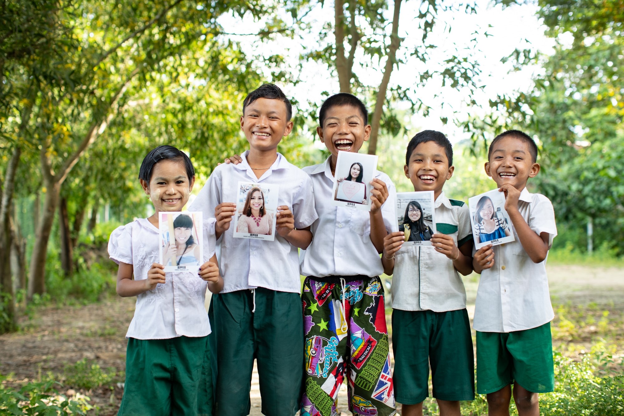 Grupo de cinco niños de Myanmar mostrando las fotos de sus padrinos y sonriendo.