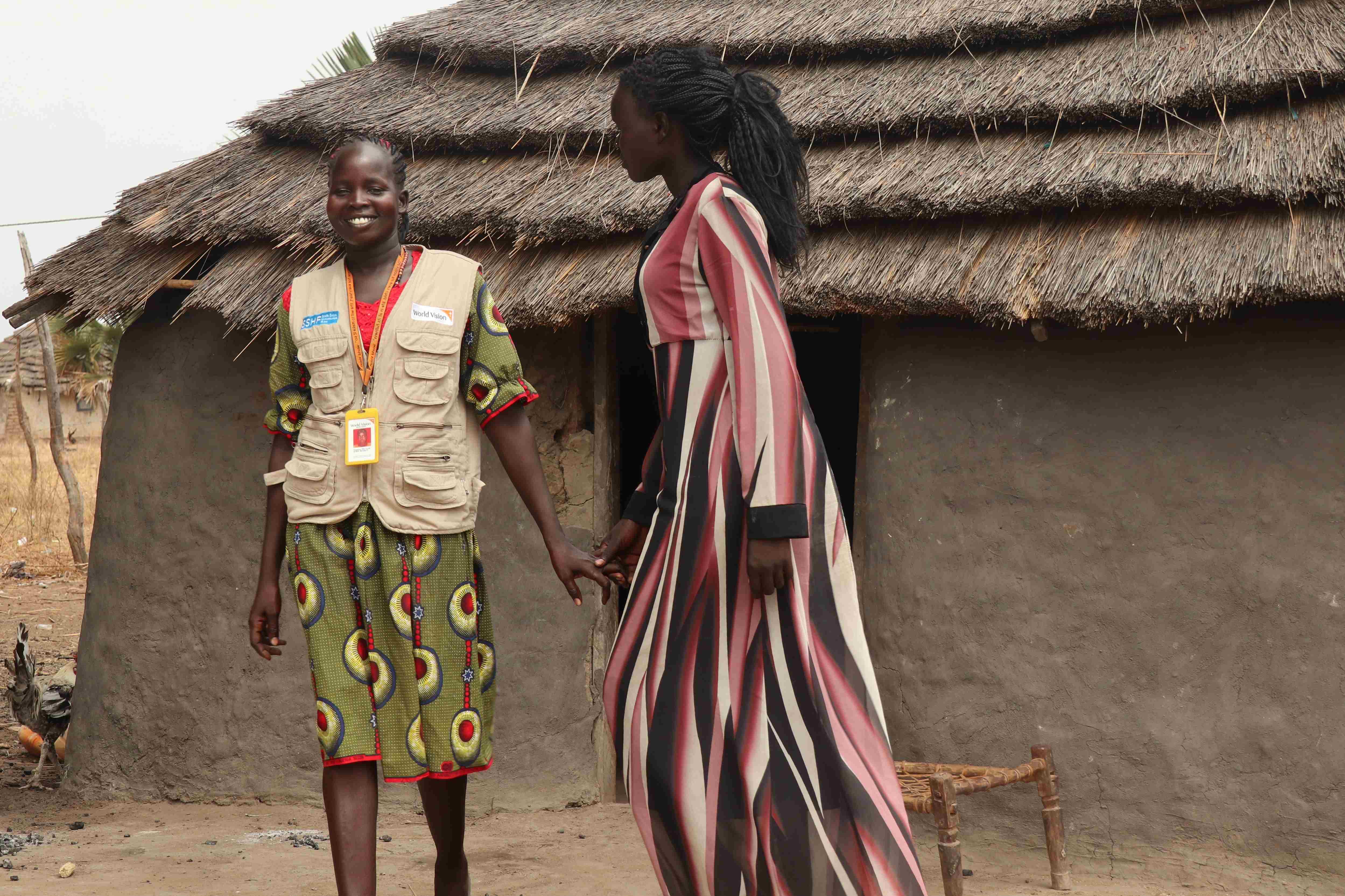 Katina y su trabajadora social de World Vision, Pasquina, sonríen y charlan frente a una casa