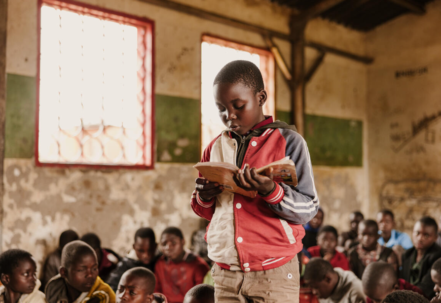 Niño de Malawi leyendo un libro delante de un aula llena de alumnos