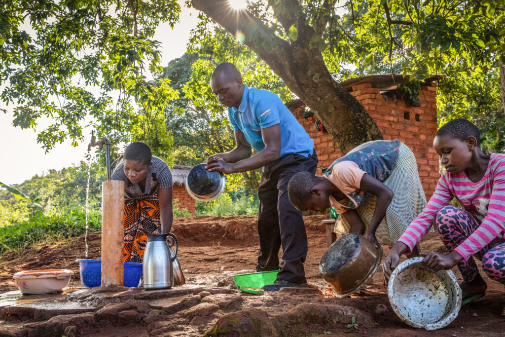 Familia lavando los platos en una nueva fuente de agua comunitaria.